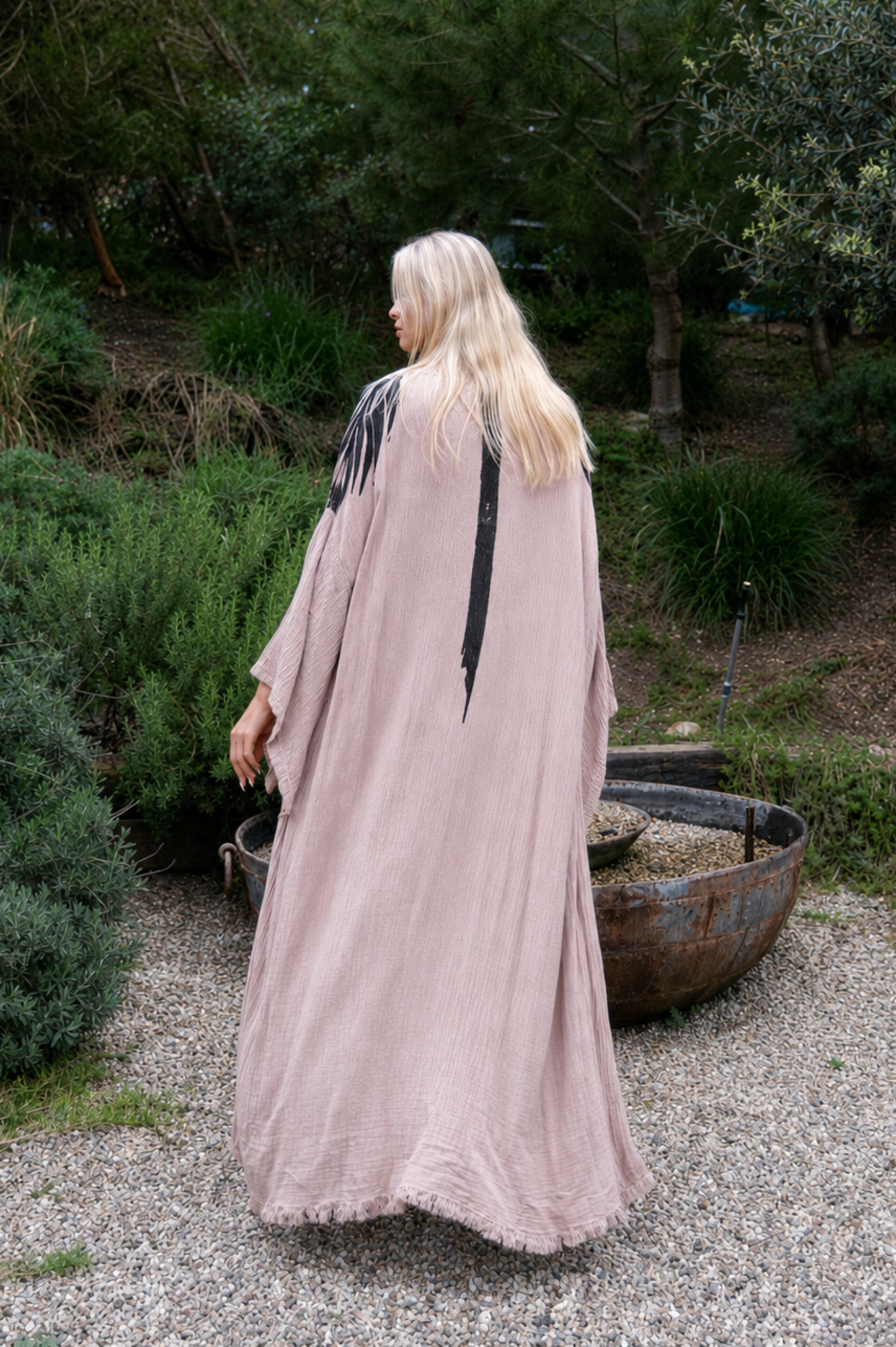 Person in a long, light-colored dress standing in a garden with greenery.