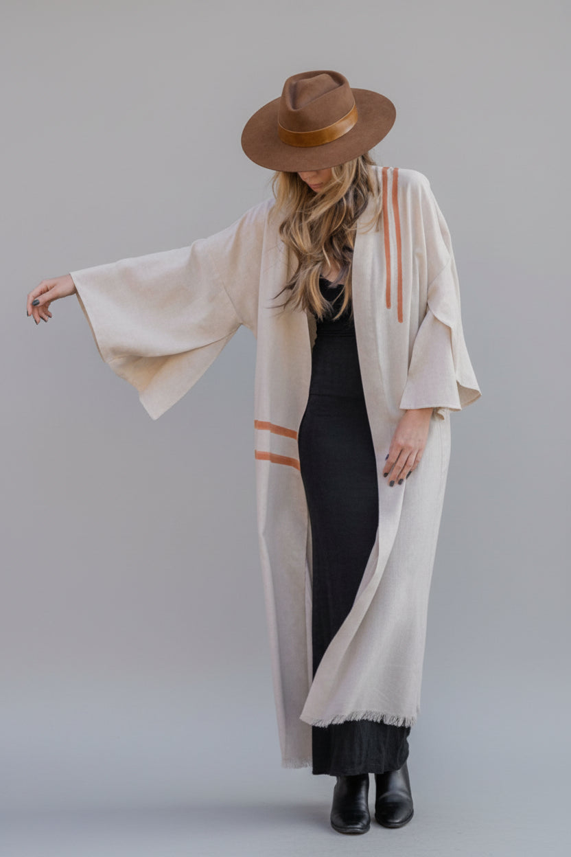 Woman wearing a house of malibu hand-painted flowy cotton linen kimono in color natural linen with apricot peach stripes