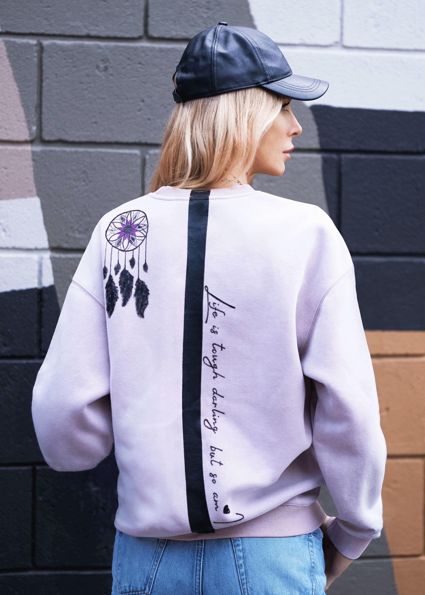 GEN Z MODEL WEARING A PURPLE SWEATSHIRT WITH QUOTE DOWN THE BACK "LIFE IS TOUGH DARLING. BUT SO AM I"