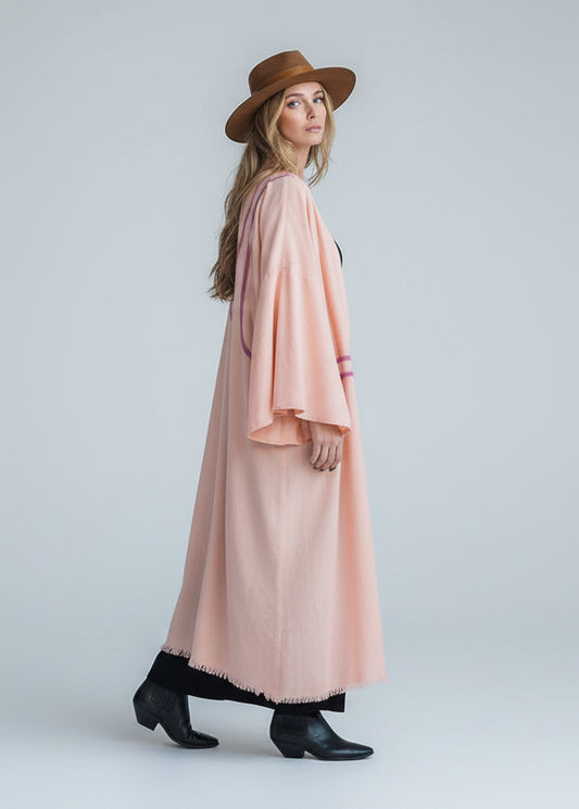 A woman wearing a light peach hand-painted flowy kimono with pleated sleeves.