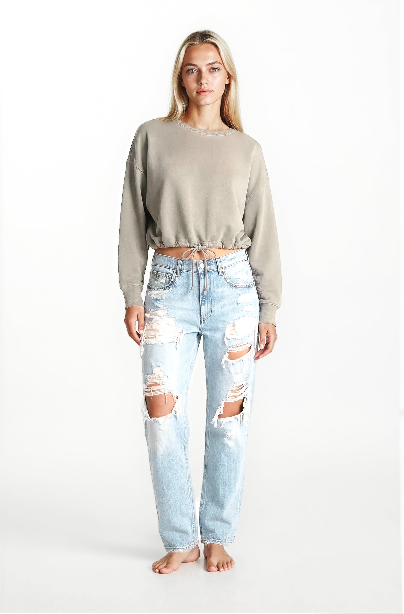 Woman wearing a sandstone cropped tie front sweater and light blue ripped jeans
