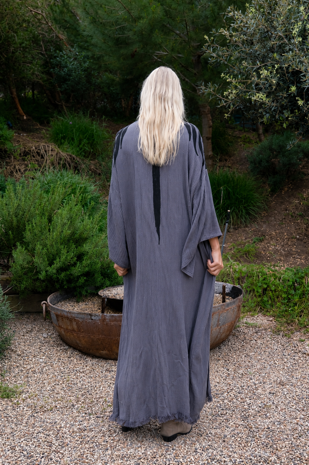 Person wearing a long, dark gray kimono robe standing outdoors with greenery in the background