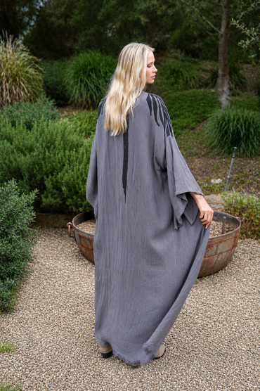 Woman in a long, dark gray kimono standing outdoors with greenery in the background