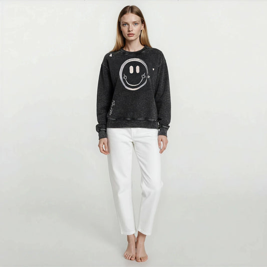 Woman wearing House of Malibu Onyx Black Vintage Wash oversized boyfriend sweatshirt with hand-drawn smiley face graphic design on front.