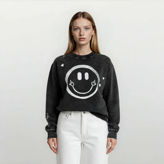 Close-up of a woman wearing an Onyx Wash oversized sweatshirt showing playful hand-drawn smiley face graphic and hearts scattered around.