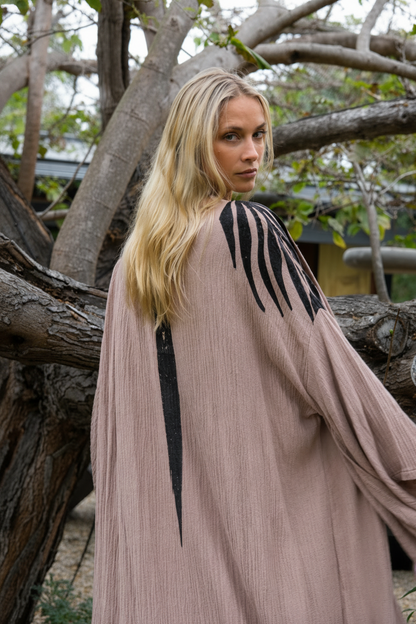 Woman wearing a long, light brown kimono with black accents in a natural setting.