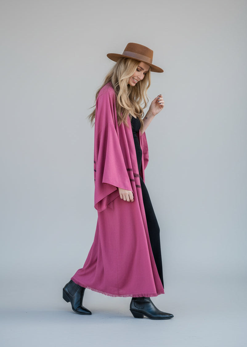Woman wearing a hand-painted long kimono in Raspberry by House of Malibu styled with a hat and over a tight black dress with boots