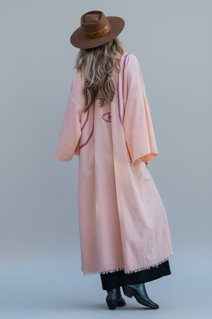 back view of a woman wearing a long peach linen kimono with hand-painted stripes  and evil eye by house of malibu 