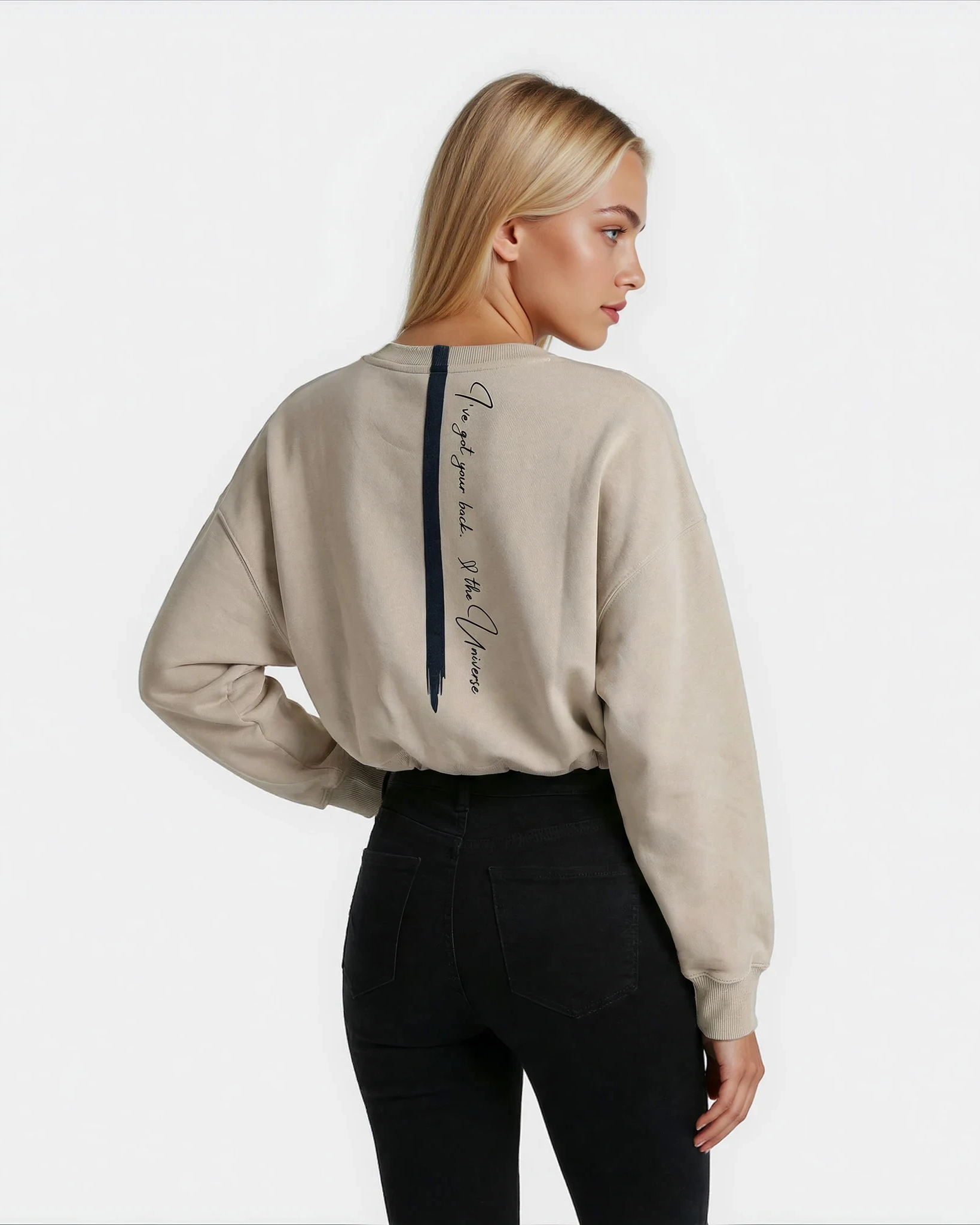 Woman wearing a beige cropped sweatshirt with an affirmation text on the back which says "Ive got your back. Love the universe"