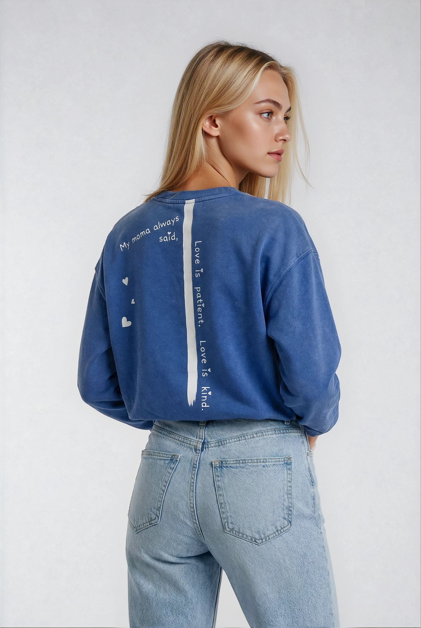 Blonde Woman wearing a blue boyfriend fit cozy sweatshirt by brand House of Malibu with hearts & "mama always said Love is patient Love is kind" printed on the back 