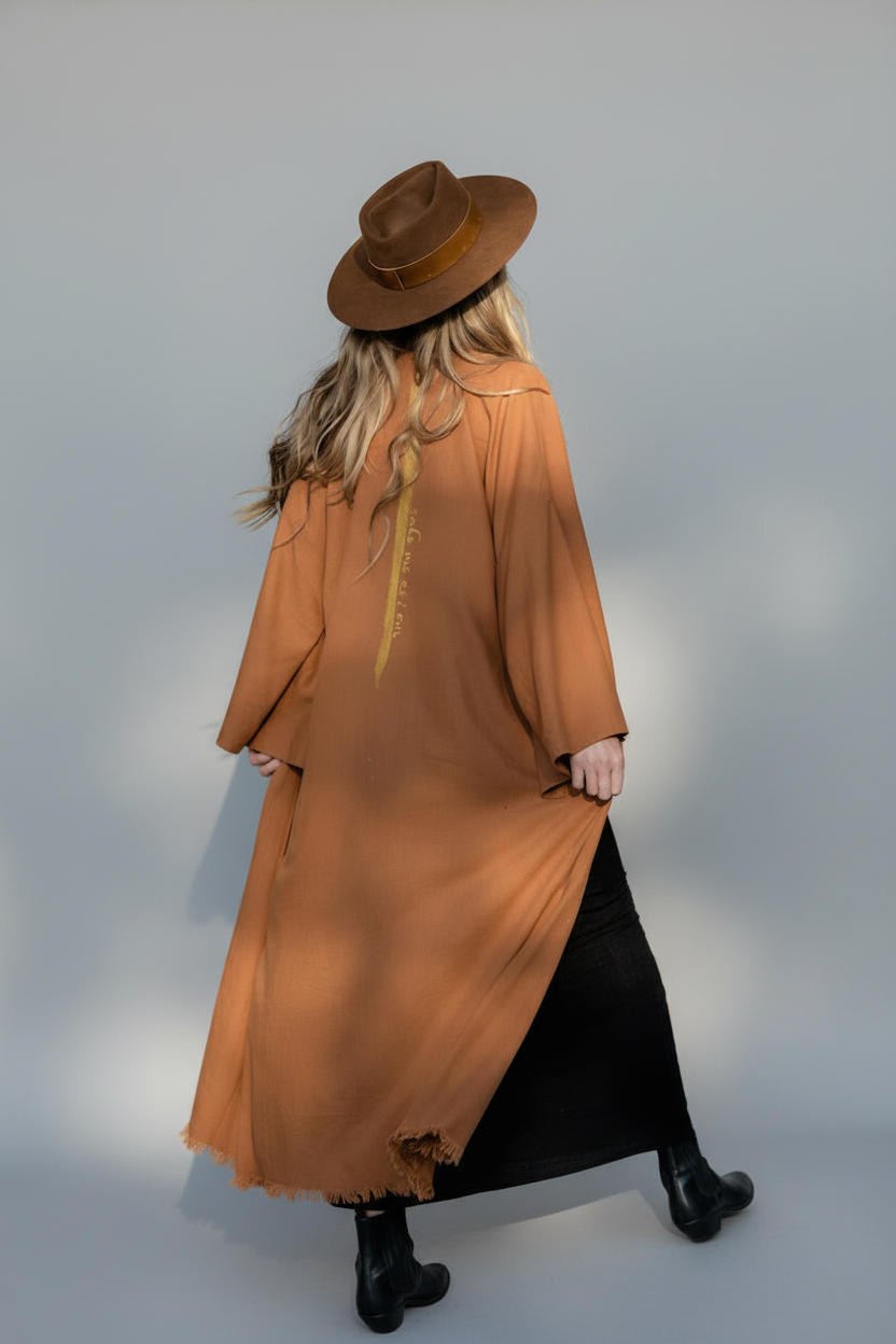 back view of a woman wearing a long camel kimono showing the lime stripe tracing her spine as a layering piece over her black dress 