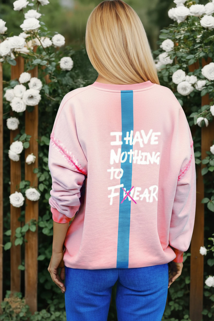 woman wearing a coral peach oversized sweatshirt  with a quote on that back that says I have nothing t fear
