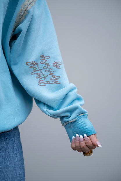 'Be Obsessively Grateful" hand-painted detail on the sleeve of light blue sweatshirt
