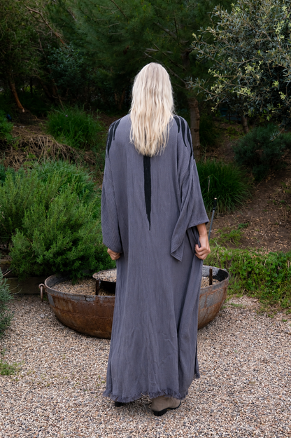Person wearing a long, dark gray kimono robe standing outdoors with greenery in the background