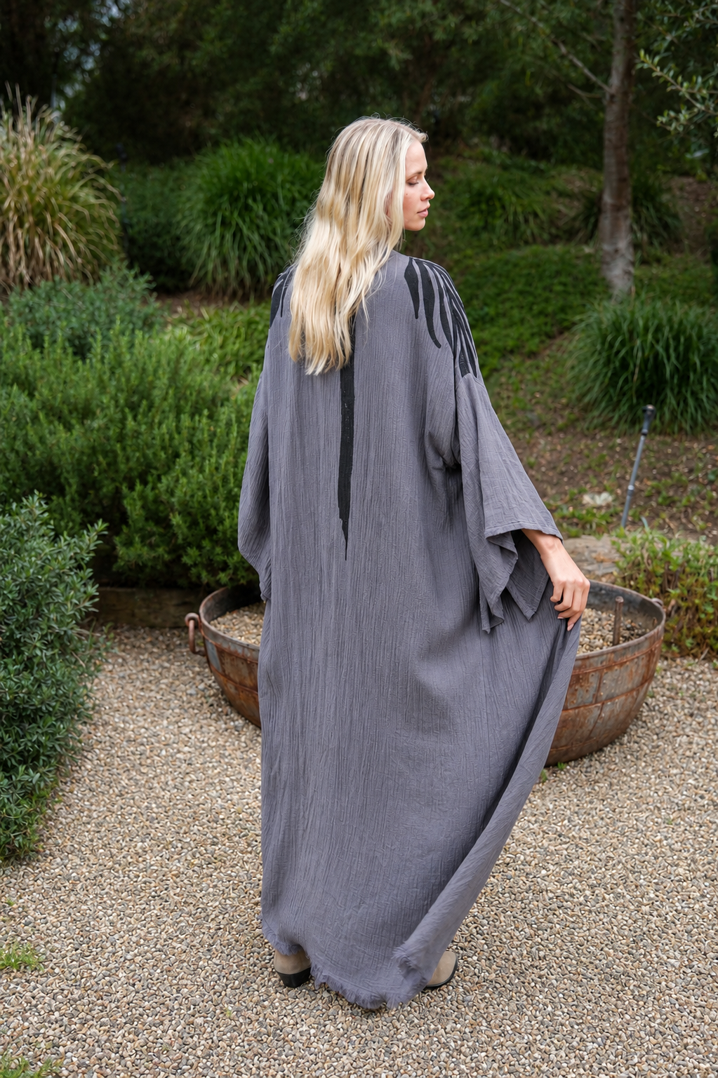 Woman in a long, dark gray kimono standing outdoors with greenery in the background