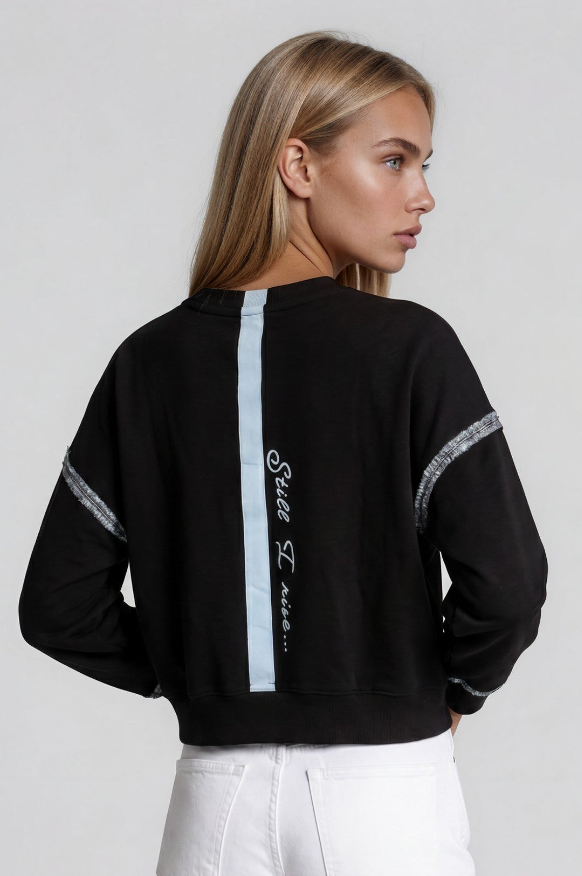 Woman wearing a black sweatshirt with hand-painted spine stripe and quote "still I rise"  