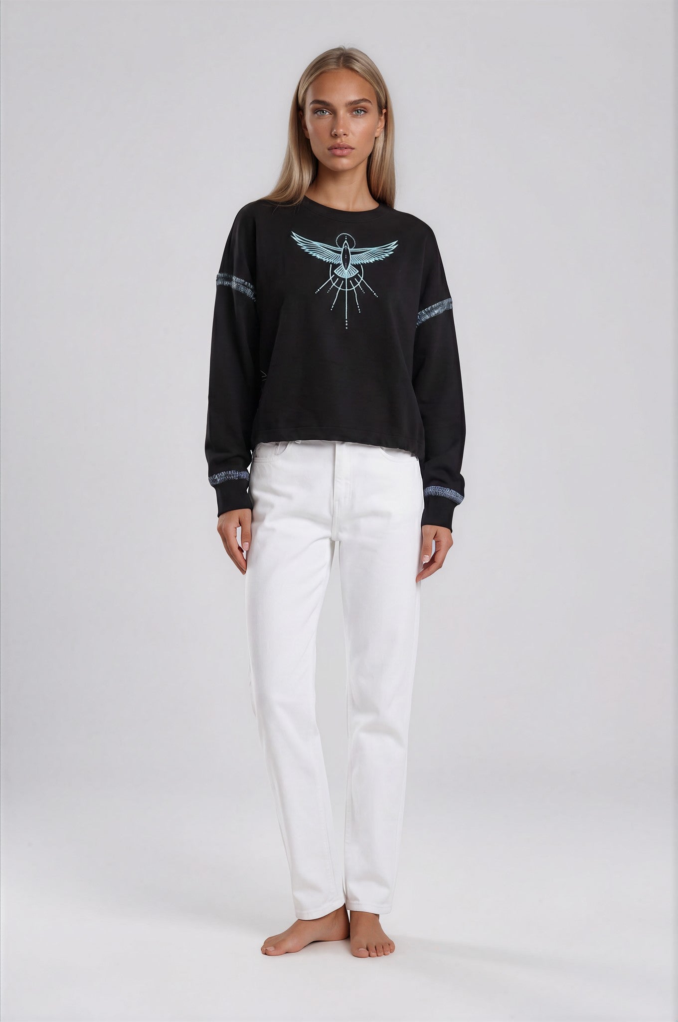 Woman wearing a black relaxed crop sweatshirt with a Phoenix Rises hand painted design and white pants