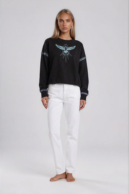 Woman wearing a black relaxed crop sweatshirt with a Phoenix Rises hand painted design and white pants