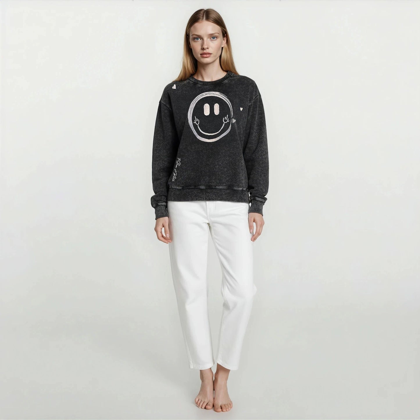 Woman wearing House of Malibu Onyx Black Vintage Wash oversized boyfriend sweatshirt with hand-drawn smiley face graphic design on front.