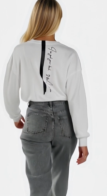 A woman is walking while  wearing a House of Malibu white cropped sweatshirt with back quoted design  detail.
